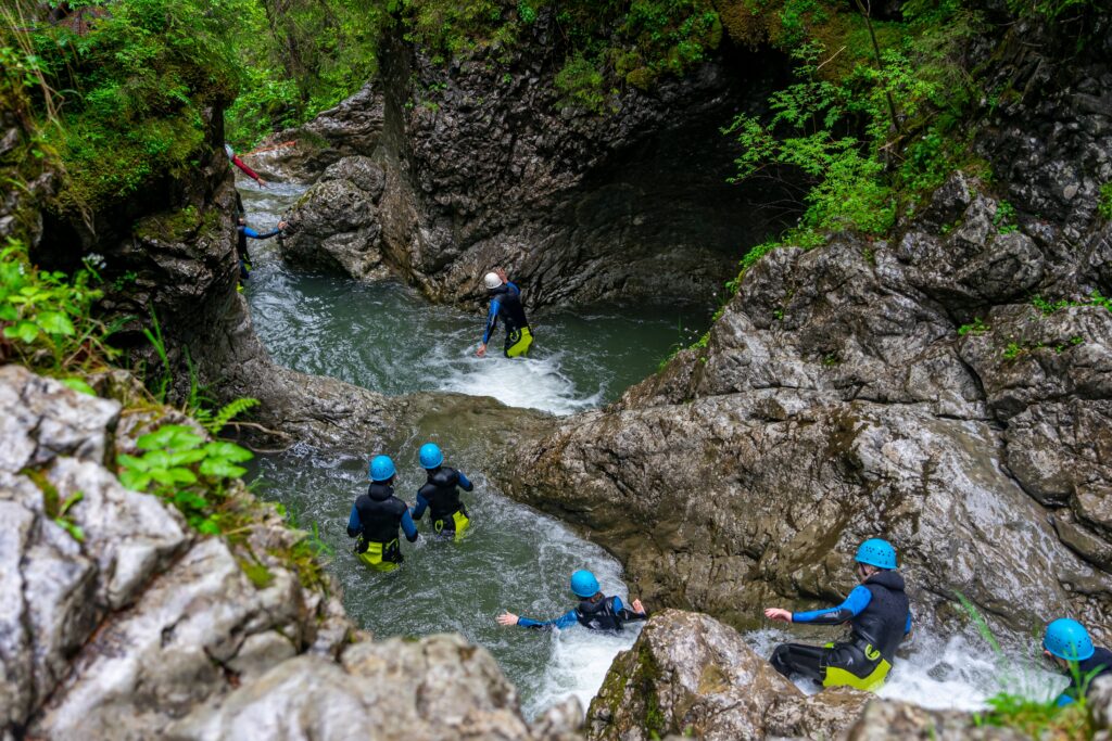Group of 7 young people in water, with safety gear on, canyoning