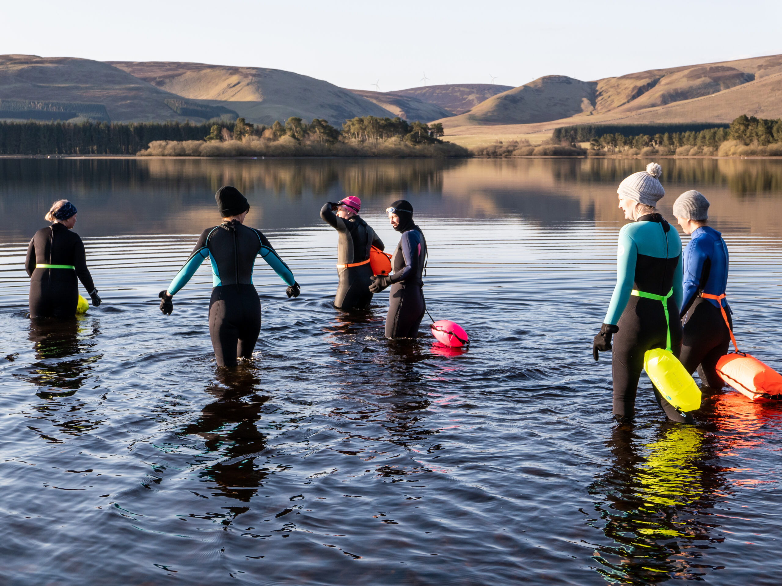 Six people in wetsuits wild swimming in a lake